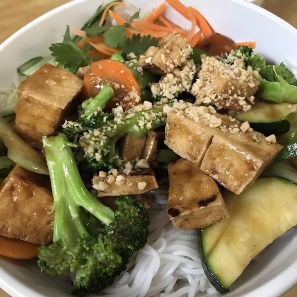 A close-up of a Phở Dollar vermicelli bowl with tofu, broccoli, carrots, zucchini, and crushed peanuts.