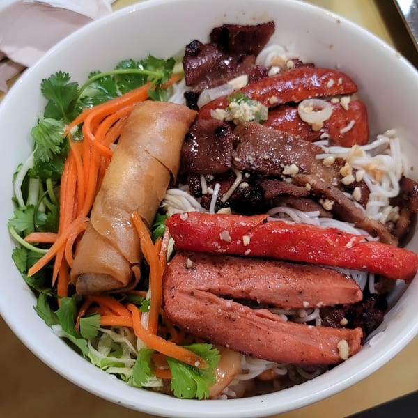 Vietnamese vermicelli bowl with grilled pork, sausage, egg roll, and fresh vegetables.