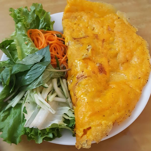 A golden Vietnamese bánh xèo pancake with a side of fresh lettuce, herbs, and shredded carrots.