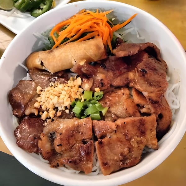 Vietnamese vermicelli bowl with grilled pork, egg roll, shredded carrots, and peanuts.